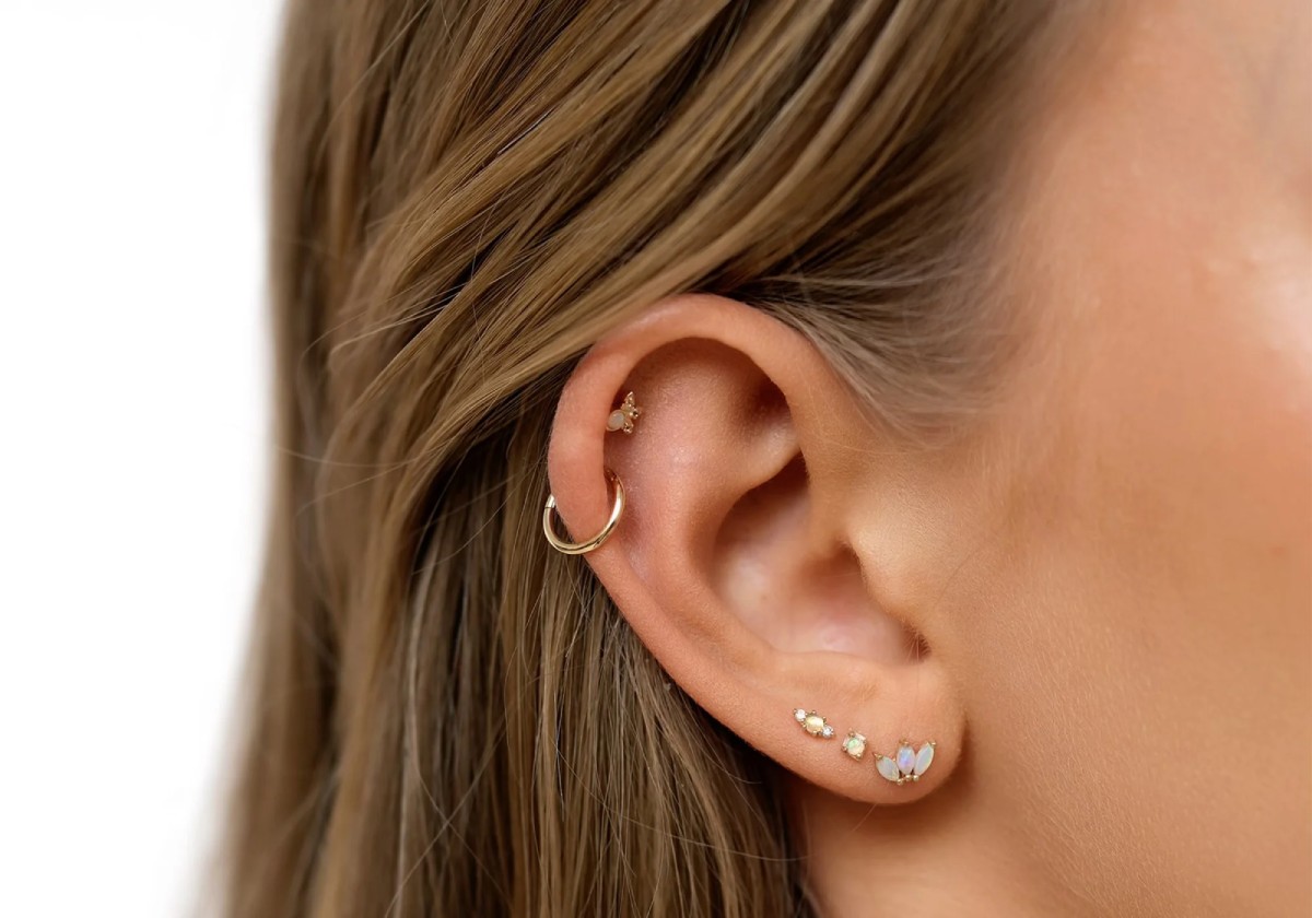 Oreille percée avec plusieurs boucles : piercing au lobe, hélix et tragus en or, illustrant les emplacements et le style des piercings tendance en 2025